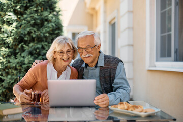 Happy senior couple using laptop and making video call while living at retirement community.