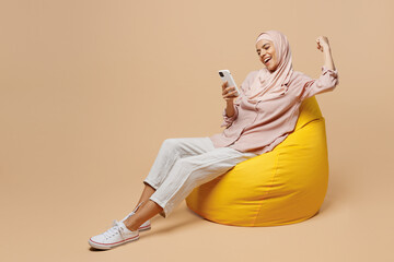 Full body young arabian asian muslim woman she wear abaya hijab pink clothes sit in bag chair use...