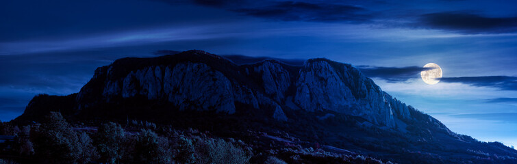 rocky formation in mountains at night. gorgeous autumn landscape in full moon light. trees on the...