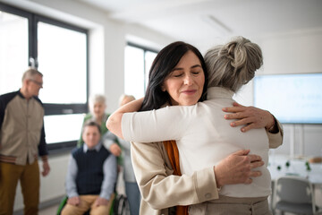 Happy senior women students meeting and hugging in classroom.