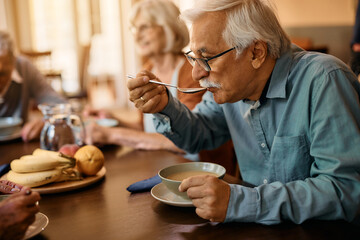 Senior man eats soup while having lunch at residential care home