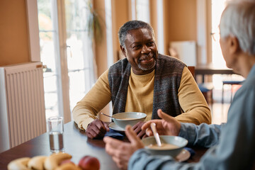 Black senior man talks to his friend during lunch at residential care home.