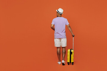 Full size back view traveler black man wear purple t-shirt hat stand with suitcase isolated on plain orange background Tourist travel abroad in spare time rest getaway Air flight trip journey concept