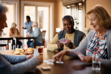 Happy black senior plays cards with friends in nursing home.