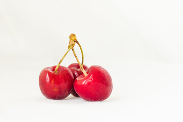 Three juicy berries of a red cherry on a white fabric background. Few red juicy cherries with stems. Two red connected sweet cherries, and one single cherry next to them. Delicious and ripe fruits