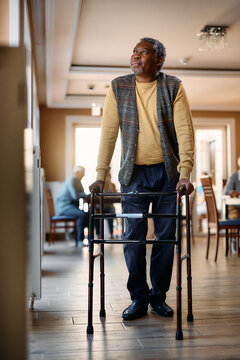 Senior Black Man Using Walker While Standing By Window At Nursing Home.