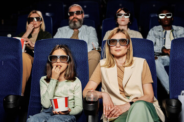 Selective focus of modern Caucasian woman and her daughter wearing polarized 3D glasses enjoying...