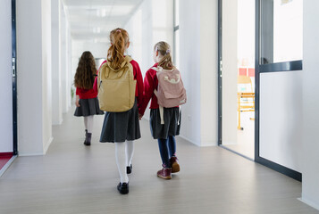 Happy schoolgirl with Down syndrome classmate in uniform walking in scool corridor with classmates,...