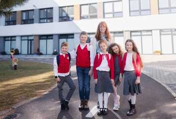 Portrait of happy schoolkids in uniforms with teacher at schoolyard, looking at camera.