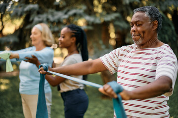 African American senior man using resistance band during exercise class in backyard of nursing home.