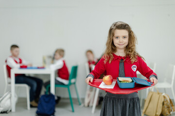 Happy schoolgrirl in uniform holding tray with lunch in school canteen.