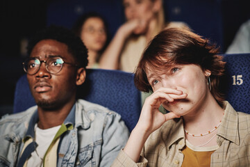 Medium close-up portrait of young Black mana and Caucasian woman spending evening together crying while watching tragedy movie at cinema - Powered by Adobe