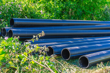 Large diameter plastic pipes for outdoor water supply. HDPE pipes lie in the field. Smooth black...