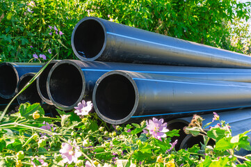 Large diameter plastic pipes for outdoor water supply. HDPE pipes lie in the field. Smooth black...