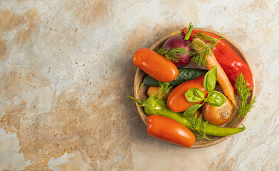 Wooden plate with fresh vegetables: green pepper, tomato, onion, carrot, cucumber, basil, dill on brown background, top view, rustic concept