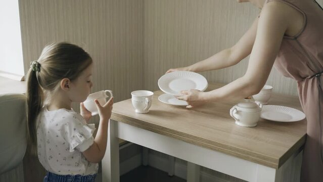 Mom and daughter put plates and cups on the table. The child helps his mother.
