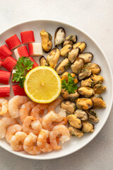 Fresh seafood charcuterie - shrimps, mussels and crab sticks in plate, bright background, top view.