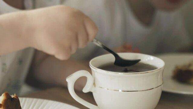 The girl stirs sugar in a mug with a teaspoon.