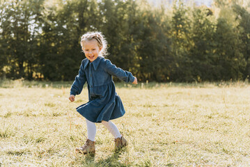 beautiful happy girl running in meadow. Beautiful warm summer evening. Little child in field. Freedom, childhood, lifestyle concept. portrait of girl smiling