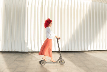 a fashionable woman with red afro hair and sunglasses rides an electric scooter going to work,...