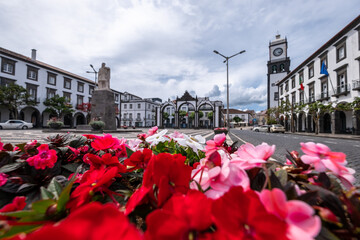 Red Flowers in selective focus with "Portas da Cidade", the city symbol of Ponta Delgada in the Background. São Miguel Island in the Azores, Portugal.