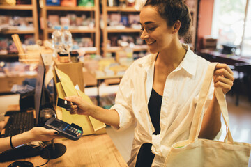 Young woman paying in a shop using credit card and terminal.