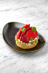 Cake with cream, strawberries and pistachios n a  plate on a marble background. Restaurant banquet menu.