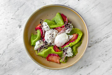 Nutritious healthy breakfast of poached eggs, spinach pancakes and salmon dyed with beets in a  plate on a marble background. Restaurant banquet menu.