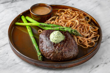 Beef steak with butter, deep-fried onions, asparagus and peanut sauce in a  plate on a marble background. Restaurant banquet menu.