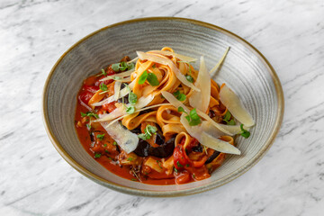 Pasta on a pillow of grilled vegetables with sauce and parmesan in a  plate on a marble background. Restaurant banquet menu.