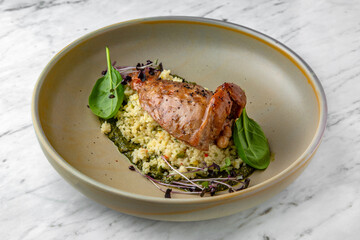 Fillet of rabbit or duck with couscous or bulgur with spinach sauce in a  plate on a marble background. Restaurant banquet menu.