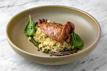 Fillet of rabbit or duck with couscous or bulgur with spinach sauce in a  plate on a marble background. Restaurant banquet menu.