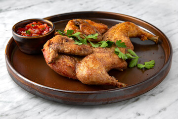 Chicken Tobacco (Tapaka) grilled whole with spicy sauce in a  plate on a marble background. Restaurant banquet menu.