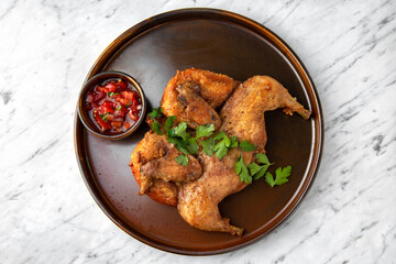 Chicken Tobacco (Tapaka) grilled whole with spicy sauce in a  plate on a marble background. Restaurant banquet menu.