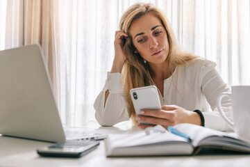 Female freelancer using smartphone on desk at home