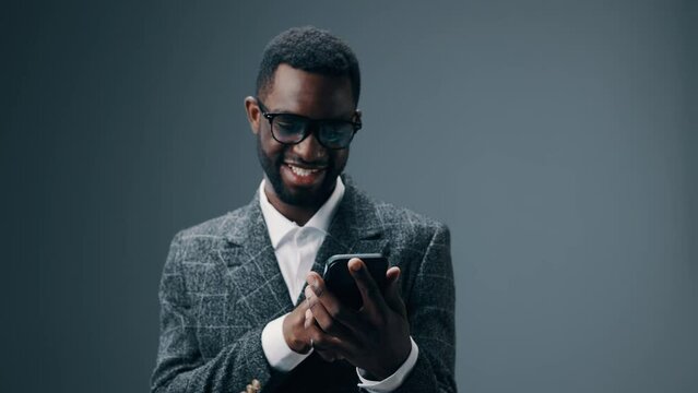 A African American businessman man holding a phone in his hands looks surprised and screams with joy and delight