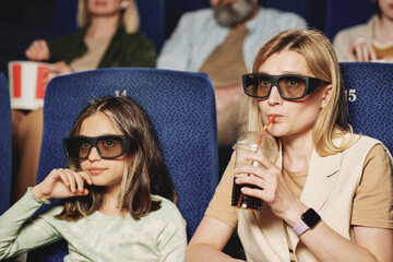 Mature Caucasian woman and her preteen daughter wearing polarized 3D eyeglasses watching film at cinema