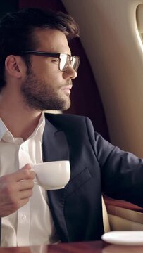 vertical video of businessman holding coffee and looking at illuminator while traveling by plane