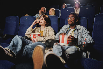 Young gen Z Black man and Caucasian woman wearing casual clothes relaxing watching movie and eating...