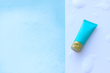 Blue cosmetic bottle shower gel on plastic board with foam bubbles background in the bathroom
