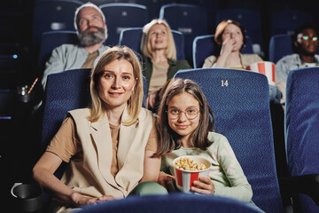 Portrait of modern Caucasian woman and her preteen daughter sitting at cinema looking at camera