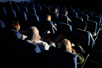 High angle view of unrecognizable people sitting in in darkness in cinema hall waiting for movie to...