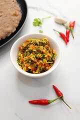 Super spicy green and red bird eye chili chutney using lal and hari mirch, garlic cloves, and coriander. served in a white bowl. Also known as Thecha in Marathi served with Raagi roti. copy space
