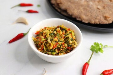Super spicy green and red bird eye chili chutney using lal and hari mirch, garlic cloves, and coriander. served in a white bowl. Also known as Thecha in Marathi served with Raagi roti. copy space