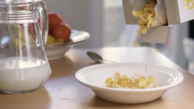 Pouring Cereal Flakes Of Corn From A Box Into A Bowl In The Morning For Breakfast, In Slow Motion