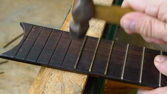 Installing frets on an acoustic guitar. A guitar luthier hammers the frets into the fretboard of an acoustic guitar.