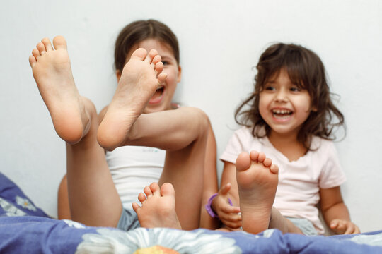 Two sisters girls are sitting on the bed and having fun showing bare feet on a white background