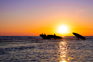 The sun sets in the sea. Three people with SUP boards are walking towards the sea against the backdrop of sunset.