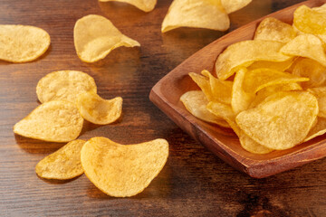 Potato chips or crisps in a bowl and scattered on a wooden background, a close-up