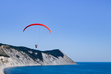 One red paraglider flies over mountains and blue sea